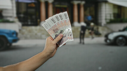 Man holding icelandic krona banknotes on a city street with blurred cars in the background outdoors...