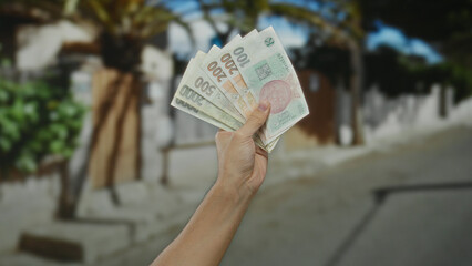 Man holding czech koruna banknotes on outdoor city street showcasing currency and economic theme.