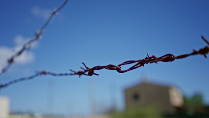 Barbed wire stretched against a clear blue sky with a distant house, capturing the essence of...