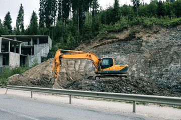 Excavator working at construction site near concrete building structure. Heavy machinery digging on...