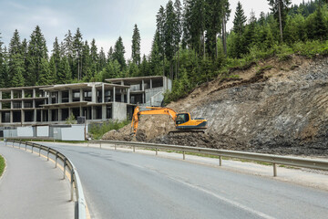 Excavator working at construction site near concrete building structure. Heavy machinery digging on...