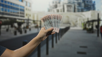 Man holding bangladeshi taka banknotes in hand on a city street illustrating financial transactions...