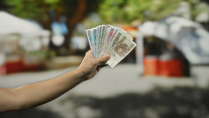 Man holding polish zloty banknotes on a city street with vibrant outdoor atmosphere, showcasing...