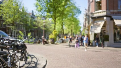 Obraz premium Blurred european city scene with people walking outside, bicycles parked, trees lined up, sunny day, urban feel, showcasing relaxed, outdoor lifestyle in blurry focus.