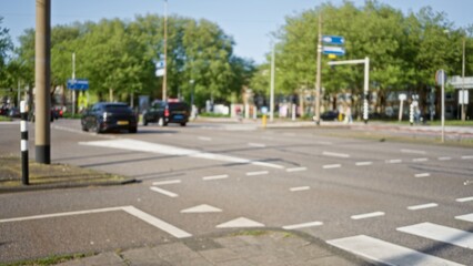 Blurred urban street scene in a european city featuring defocused cars, road markings, and greenery in the warm sunlight.