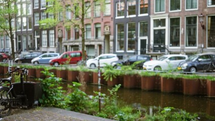 Blurred view of amsterdam canal lined with cars and traditional buildings, showcasing defocused...