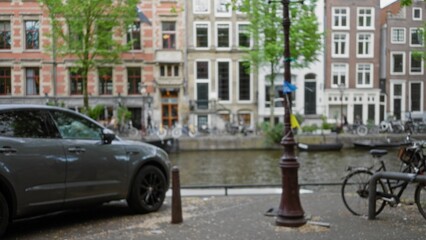 Blurred view of amsterdam canal with defocused car and bicycles lining the picturesque waterway in...
