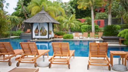 Blurred tropical resort pool area with wooden loungers, palm trees, and a luxury cabana in the...