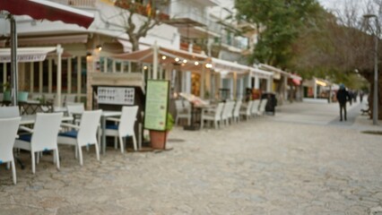 Obraz premium Defocused promenade in mallorca with blurred chairs and tables lining a mediterranean walk under soft lighting, depicting a peaceful and inviting outdoor dining scene.