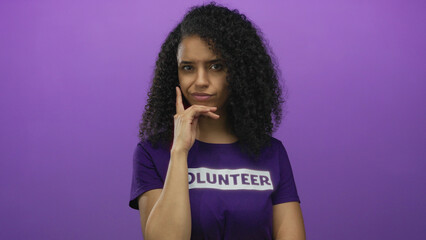 Young hispanic woman wearing a volunteer shirt stands against an isolated purple background,...