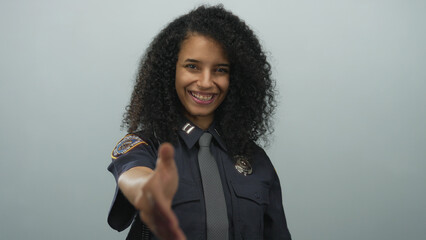 Hispanic policewoman in uniform extends a handshake, smiling confidently against a white background.