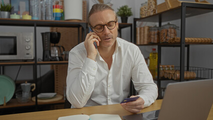 Mature man with glasses talking on phone while examining credit card in modern office setting...