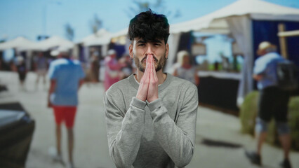 Young man with hands in prayer gesture on busy outdoor market street background showcasing vibrant...