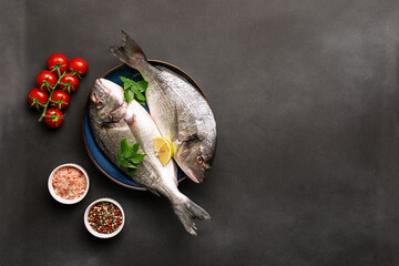 Raw dorado fish with spices, cherry tomatoes and Himalaya salt on the ceramic plate on black stone...