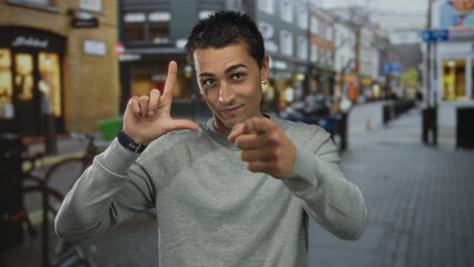 Young hispanic man making loser gesture with hand and pointing at camera in busy urban street;...