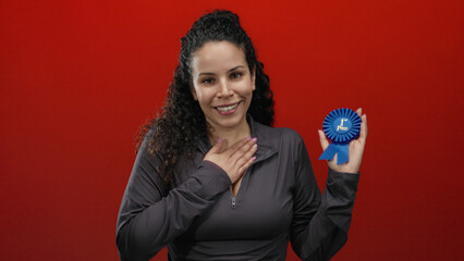 Hispanic woman proudly holding a first-place ribbon against a bold red background, conveying joy...