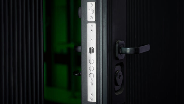 Close-up of a half-open armored door revealing a robust metal lock and handle against a dark, mysterious background. Photo