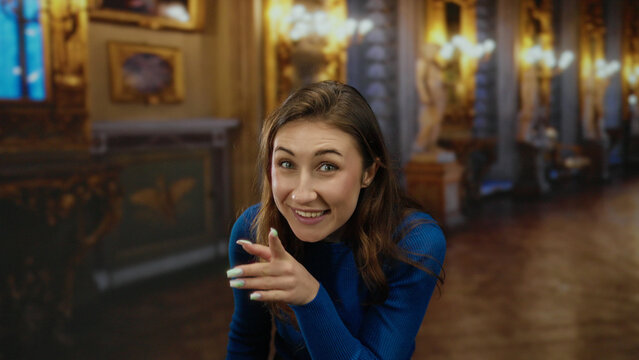 Woman in blue sweater sharing secret in elegant museum interior, her expression playful and intriguing, surrounded by classical art and luxurious decor, indoor setting.