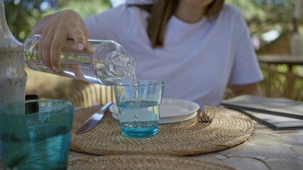 Woman pouring water into a glass at an outdoor mediterranean restaurant setting with wicker...