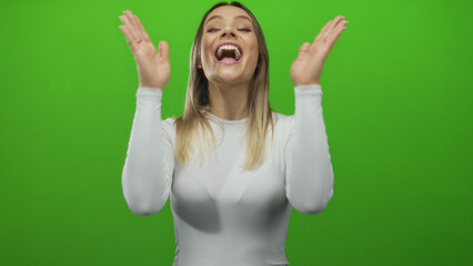 Young blonde woman smiles enthusiastically against an isolated green background, highlighting her...