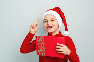 Cheerful boy in Santa hat holding an envelope, postcard, greeting, letter to Santa Claus ,...