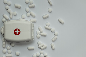 White pill box with medical cross symbol and pills next to it, white horizontal background