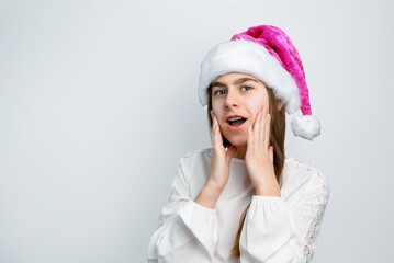 Cheerful little girl in Santa hat showing joy, delight, surprise, approval. Happy emotions, joy of...