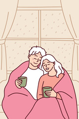 Elderly couple sits closely under warm blanket on Christmas night holding hot tea mugs, sharing peaceful and loving moment in cozy home setting