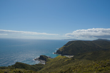A vast coastal landscape features a long sandy beach, a turquoise ocean with distant islands, and...