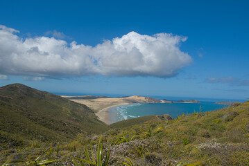 A vast coastal landscape features a long sandy beach, a turquoise ocean with distant islands, and...