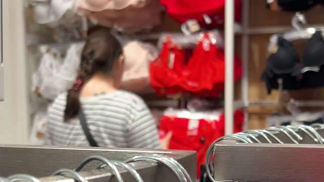 Horizontal defocused 4K video. Shelf in foreground. Out of focus woman chooses red lingerie, bra in female clothing store. Concept of sale, retail shop, Black friday, buying clothes, promo. Blur
