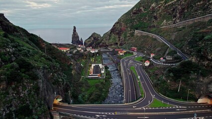 A highway and a mountain river in a valley among the mountains. The road to Madeira leads to the ocean. View from the drone