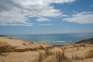 A vast coastal landscape features a long sandy beach, a turquoise ocean with distant islands, and...