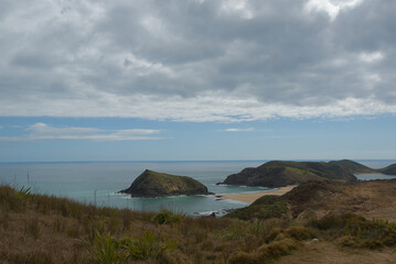 A vast coastal landscape features a long sandy beach, a turquoise ocean with distant islands, and...