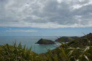 A vast coastal landscape features a long sandy beach, a turquoise ocean with distant islands, and...