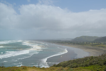 A vast coastal landscape features a long sandy beach, a turquoise ocean with distant islands, and...