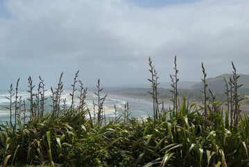 A vast coastal landscape features a long sandy beach, a turquoise ocean with distant islands, and...