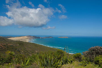 A vast coastal landscape features a long sandy beach, a turquoise ocean with distant islands, and...