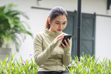 Fit and healthy Asian woman using smart phone after doing exercise in the park. Female jogger....