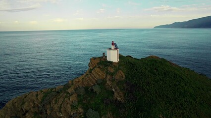 The drone flies around the lighthouse on top of the cliff. A rock in the sea near the seashore. A...