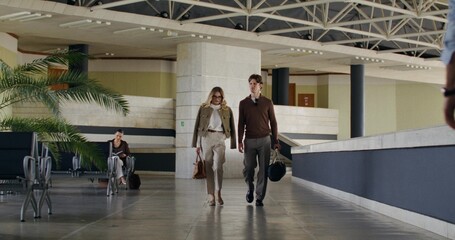 A man and a woman talk as they walk through the waiting room at a train station or airport