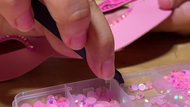 Horizontal defocused video close up. Female hand gluing glitter plastic rhinestones on leather pink magenta cat mask on table. DIY craft art work. Woman in workshop. Diverse beauty, skill, hobby, gift