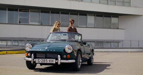 A man and a woman put their bags in the trunk of a retro car and get in the car
