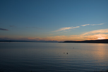Serene Lake Taupo at dusk, with soft pastel hues reflecting on the calm water, capturing a peaceful...