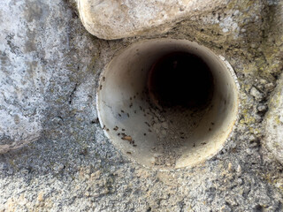 Close-up of round pipe in concrete wall showing signs of erosion and dirt accumulation
