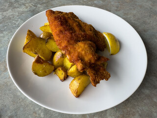 Crispy fried fish with roasted potatoes and lemon on white plate
