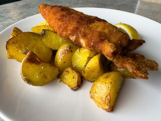 Golden fried fish with roasted potatoes and lemon on a white plate