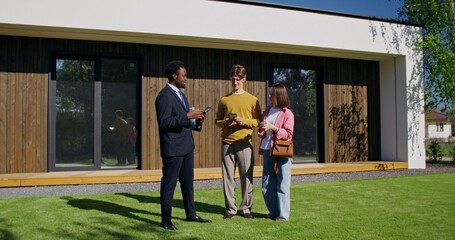 A young couple wants to buy a house. They're talking to a realtor standing in the backyard on a summer day.
