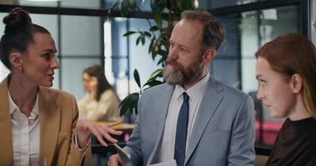 A group of stylish people are talking while sitting at a table and discussing documents in the office. Woman uses a laptop
