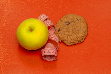 Fresh organic apple fruit next to baked cookie with tape measure in the middle